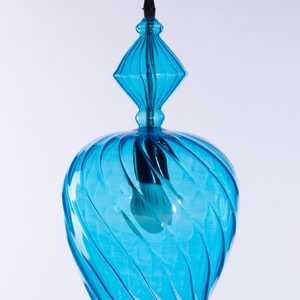 May include: A blue glass pendant light with a swirling design. The light has a diamond-shaped top and a round bottom.