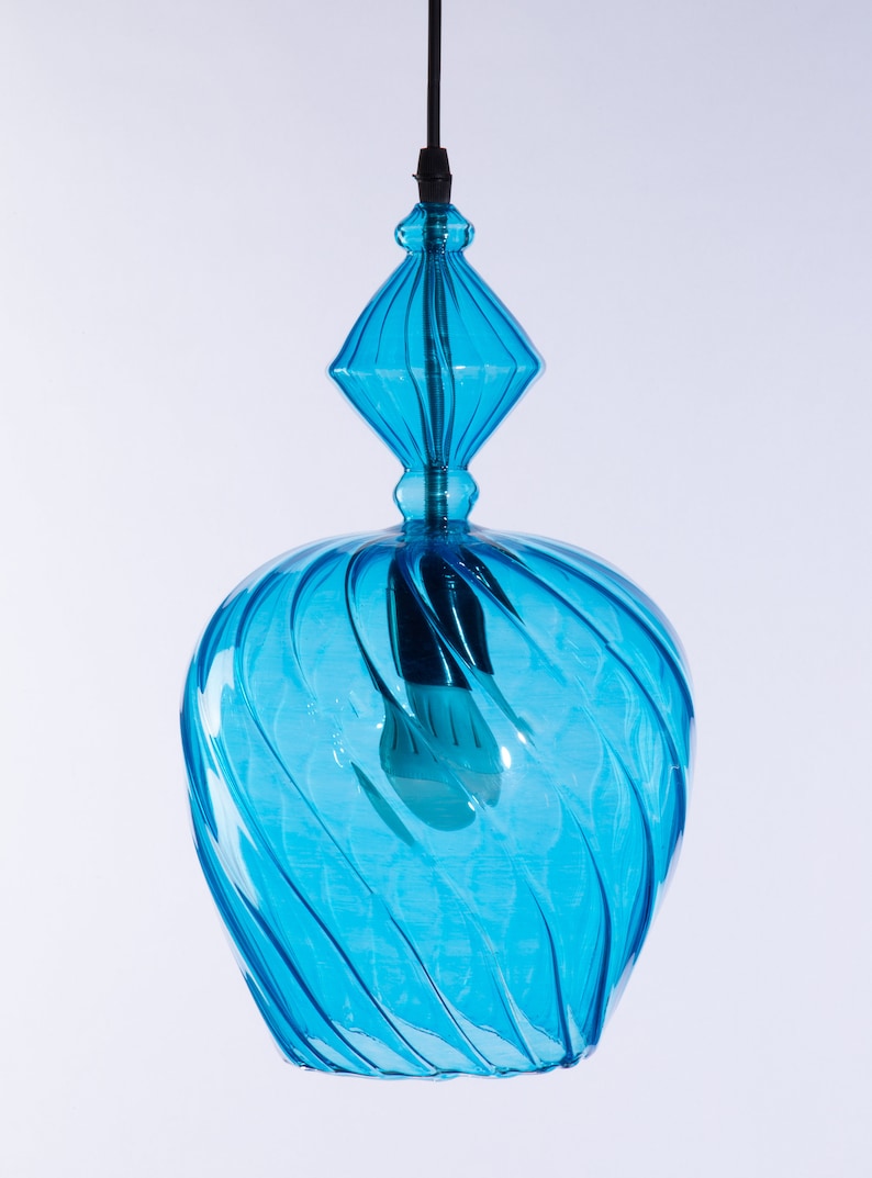 May include: A blue glass pendant light with a swirling design. The light has a diamond-shaped top and a round bottom.