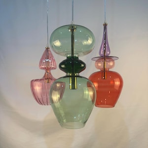 May include: Three glass pendant lights with different shapes and colors. The lights are hanging from the ceiling and are made of clear glass with a variety of colors, including pink, green, and red.