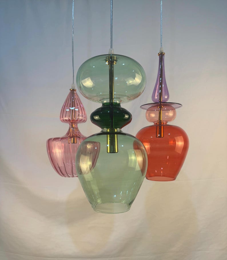 May include: Three glass pendant lights with different shapes and colors. The lights are hanging from the ceiling and are made of clear glass with a variety of colors, including pink, green, and red.