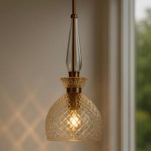 May include: A pendant light fixture with a clear glass, teardrop-shaped top and a diamond-patterned, amber-colored glass shade. The fixture has a brass-colored metal finish and is suspended from a matching rod.