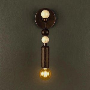 Könnte beinhalten: Moderne Wandleuchte mit dunkler Bronzeoberfläche. Das Design umfasst eine kreisförmige Rückplatte, eine Reihe von kugelförmigen Akzenten in Weiß und Dunkelbraun sowie einen zylindrischen Körper. Unten befindet sich eine warme, leuchtende Glühbirne.