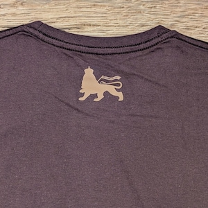 May include: A dark gray t-shirt with a lion silhouette graphic on the back. The lion is wearing a crown and holding a flag.