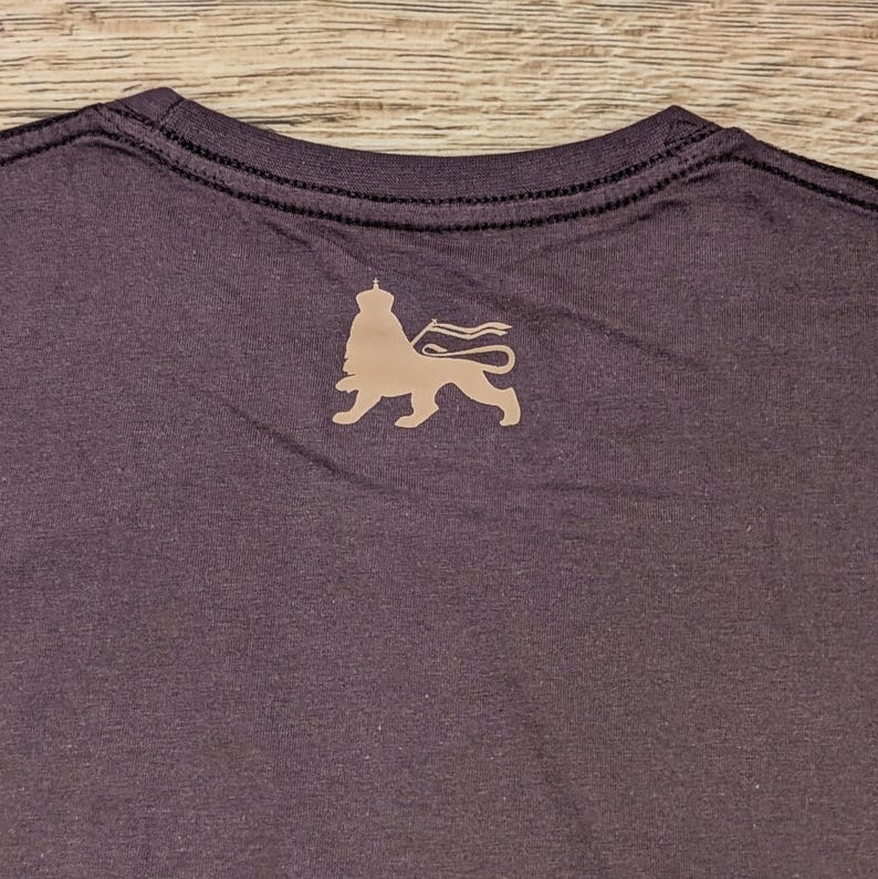 May include: A dark gray t-shirt with a lion silhouette graphic on the back. The lion is wearing a crown and holding a flag.