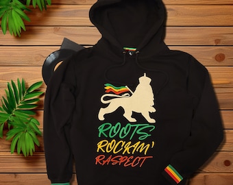 May include: A black hooded sweatshirt featuring a graphic of a lion wearing a crown and holding a flag with red, yellow, and green stripes. Below the lion, the text reads ROOTS, ROCKIN', RASPECT in green, yellow, and red. The cuffs and hem have stripes.