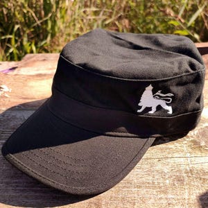 May include: A black military style cap with a white embroidered lion design on the front.