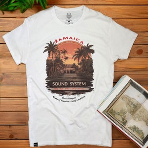 Può includere: Maglietta bianca con un design grafico di una scena di tramonto con palme e il testo "Jamaica One Love - Irie Vibes Only" e "Sound System Much Respect Beats of Freedom Unity's Anthem".
