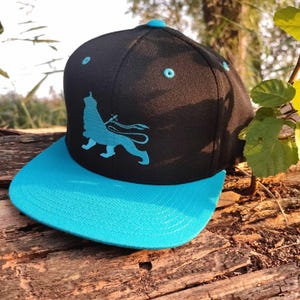 May include: A black and turquoise blue baseball cap with a lion silhouette embroidered on the front.