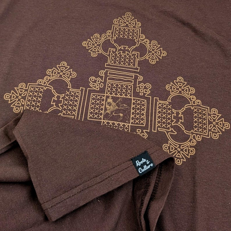 May include: A brown t-shirt with a gold geometric design featuring a lion. The shirt has a tag that reads "Roots & Culture".