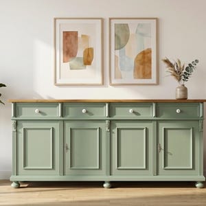 Könnte beinhalten: Ein salbeigrünes Sideboard aus Holz mit vier Schubladen mit weißen runden Knöpfen und vier Schranktüren mit Kassettenfronten. Das Möbelstück hat eine Oberfläche aus Naturholz und steht auf kleinen kugelförmigen Füßen.