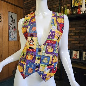 May include: A colorful Halloween-themed vest with a patchwork design. The vest features various Halloween motifs, including pumpkins, witches, bats, and spiders, set against a background of purple, yellow, and blue squares. It has a V-neck and button closure.