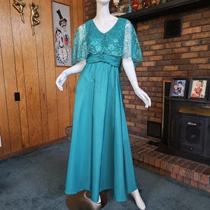 May include: A teal blue maxi dress with a lace overlay bodice and short sleeves. The dress has a fitted bodice and a flowing skirt.