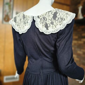 May include: A black long-sleeved dress with a large white lace collar. The dress has a fitted bodice and a full skirt.