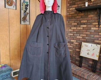 May include: A dark gray cape with a bright pink hood and trim. The cape has two front pockets and a button-up closure. The mannequin is wearing the cape.