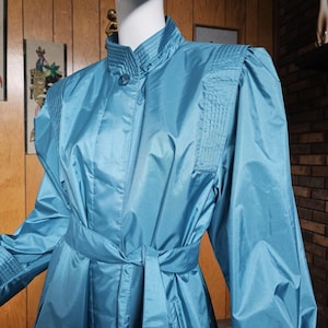 May include: A teal blue raincoat with a mandarin collar, long sleeves, and a tie belt. The raincoat has a shiny, satin-like finish.