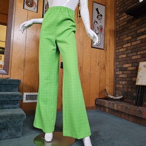 May include: Bright green, high-waisted pants with a white grid pattern. The pants have a flared leg design and an elastic waistband. The pants are displayed on a mannequin. The pants are a vibrant, eye-catching piece of clothing.