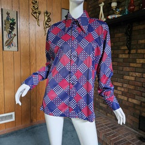 May include: A long-sleeved button-down shirt with a geometric pattern of red and blue diamonds, accented with white polka dots. The shirt has a pointed collar and is displayed on a mannequin.