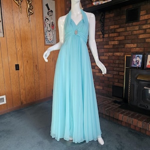 May include: A light blue halter-style gown with a jeweled embellishment at the neckline. The gown is made of a flowing, sheer fabric and has a fitted bodice and a full skirt.