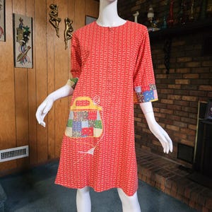 May include: A vintage red dress with a vertical white floral pattern. The dress features a patchwork pocket and cuffs with a variety of colorful fabric squares. The dress has three-quarter sleeves and a round neckline.