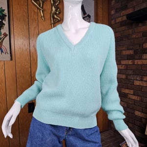 May include: A light mint green long-sleeve sweater featuring a V-neckline and a thick ribbed knit texture. The garment has long sleeves with ribbed cuffs and a ribbed hemline, providing a structured fit on the white mannequin torso.