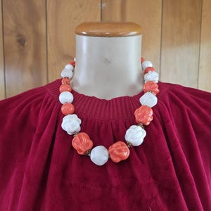 May include: A white and orange beaded necklace with large, round beads. The beads are shaped like flowers and have a textured surface.
