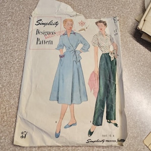 May include: Vintage Simplicity Designer's Pattern envelope featuring illustrations of two women's outfits. One woman wears a light blue wrap dress, the other a striped shirt and green pants. The envelope is off-white with red and black text.