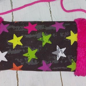 Könnte beinhalten: Eine kleine, rechteckige Umhängetasche mit schwarzem Hintergrund und buntem Sternmuster. Die Tasche hat einen leuchtend rosa, flauschigen Besatz an den Seiten und einen passenden rosa Seilriemen.