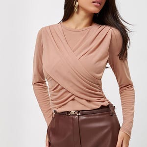 May include: A woman wearing a long-sleeved, light brown, criss-cross top with a brown leather skirt and a gold belt.