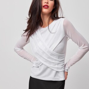 May include: A white long-sleeved shirt with a criss-cross design in the front. The shirt is made of a sheer fabric and has a relaxed fit.