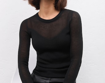May include: A long-sleeved black sweater featuring a sheer, fine-knit texture with a solid black camisole underneath, paired with black faux leather trousers that have a smooth, semi-gloss finish and a visible front button and zipper closure.