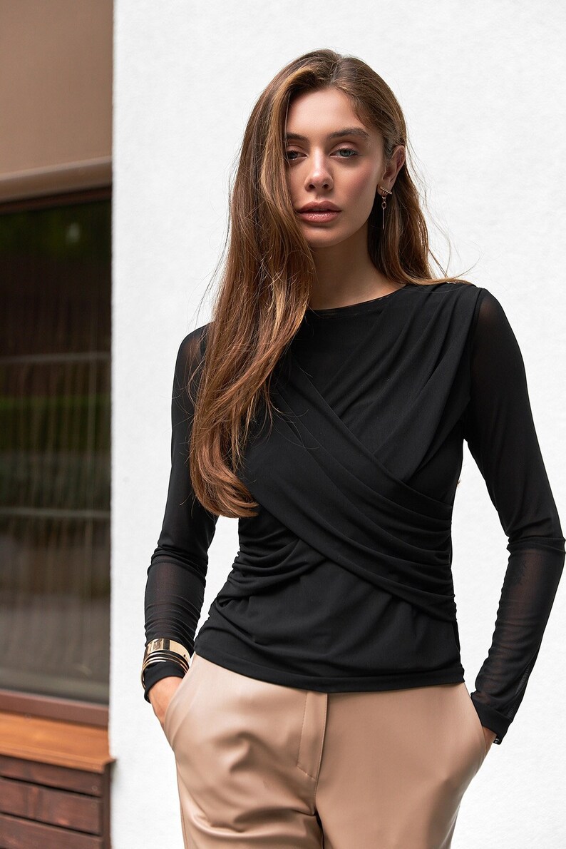 May include: A black long-sleeved shirt with a criss-cross design in the front. The shirt is made of a sheer fabric and has a relaxed fit.