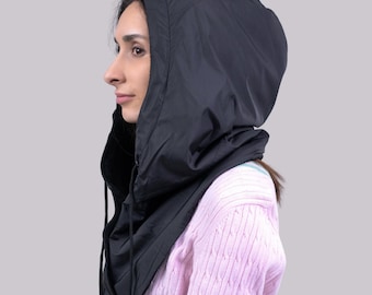 May include: Black hooded balaclava with a drawstring closure. The hood is made of a smooth, shiny material and is designed to cover the head and neck. The balaclava is shown on a person wearing a pink sweater.