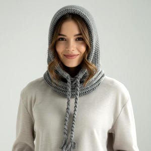 May include: A gray, knitted hood with a drawstring closure and tassels. The hood is designed to be worn around the neck and head, providing warmth and protection from the elements. The knitted texture is visible, and the hood appears to be made of a soft, comfortable material.
