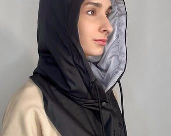 May include: A black hood with a drawstring closure and snap buttons. The hood's interior is a light gray color, providing a contrast to the black exterior. The hood is designed to be worn around the neck and head.