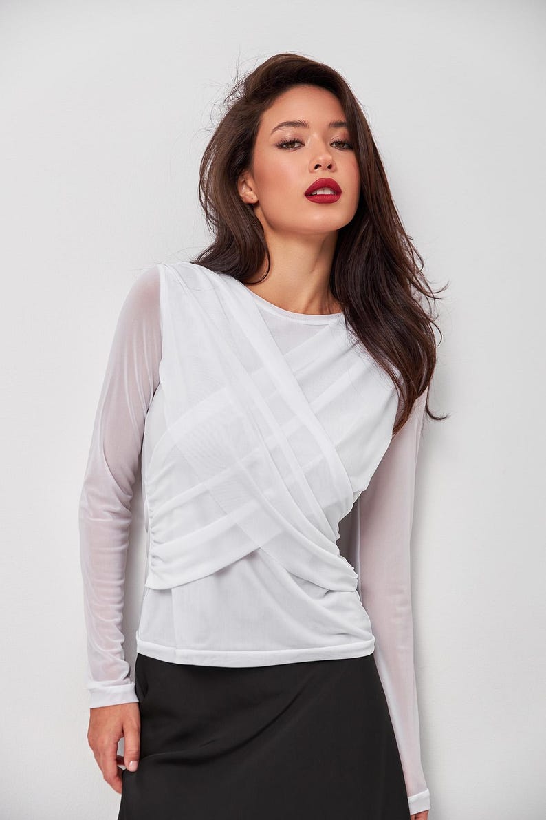May include: A white long-sleeved mesh top with a criss-cross design in the front. The top is semi-sheer and has a relaxed fit.