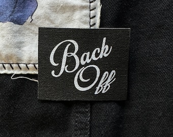 May include: Black fabric patch with white text that reads "Back Off" in a cursive font.