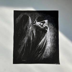 May include: Black and white illustration of a cloaked figure with a skull face. The artwork is on a black fabric, with the figure's form and details rendered in white. The image has a gothic or horror theme.