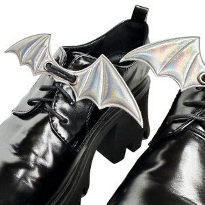 K&ouml;nnte beinhalten: Ein Paar schwarze Lederschuhe mit schimmernden Fledermausfl&uuml;gel-Schuhschmuck, der an den Schn&uuml;rsenkeln befestigt ist.