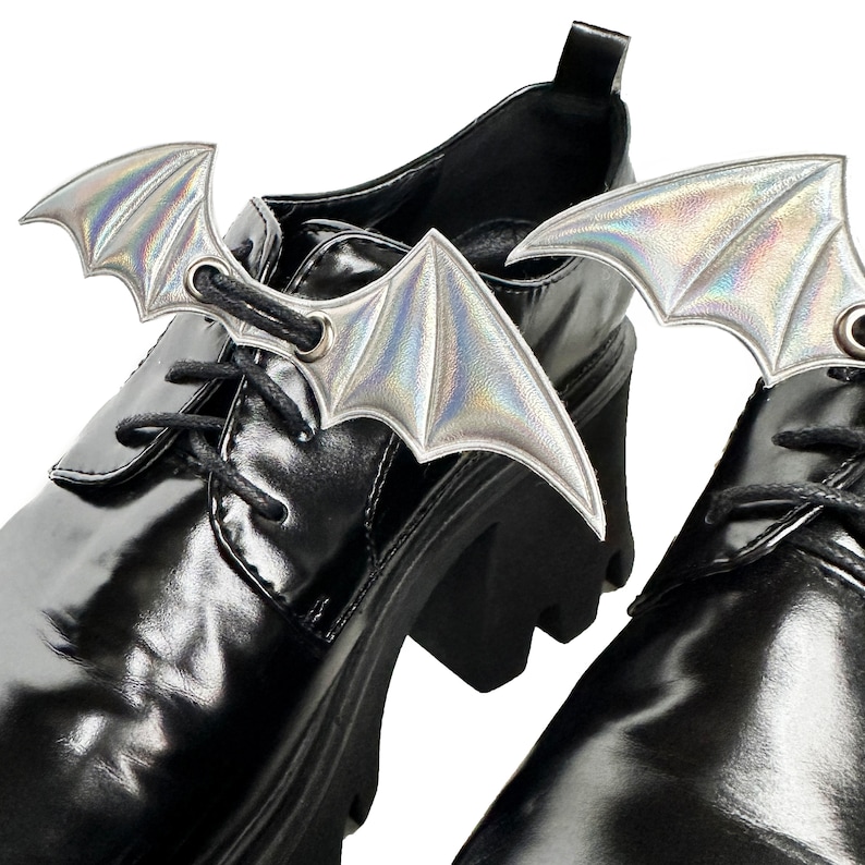 K&ouml;nnte beinhalten: Ein Paar schwarze Lederschuhe mit schimmernden Fledermausfl&uuml;gel-Schuhschmuck, der an den Schn&uuml;rsenkeln befestigt ist.