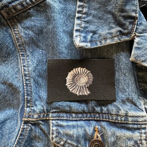 May include: A black fabric patch with a white image of a nautilus shell.