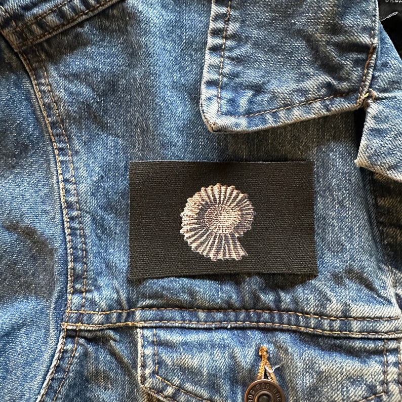 May include: A black fabric patch with a white image of a nautilus shell.