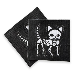 May include: Two black fabric patches with a white skeleton cat design. The cat is wearing a hat and has a smiling face.