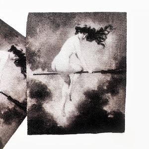 May include: Two square fabric patches with a sepia-toned image of a figure riding a broomstick through clouds. The image is a vintage-style illustration, with the figure's hair flowing in the wind. The patches are set against a white background.