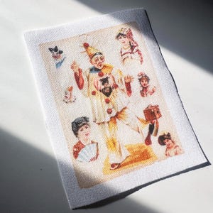May include: Rectangular fabric with a vintage print featuring a central figure in a clown costume, surrounded by smaller portraits of people. The clown wears a cream-colored outfit with red accents and a tall hat. The print has a faded, antique aesthetic.