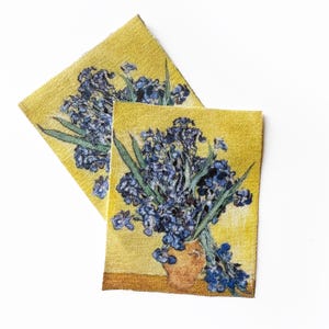 May include: Two rectangular fabric patches featuring a floral still life painting. The artwork depicts a bouquet of blue flowers in a brown vase against a yellow background. Green leaves are also visible. The patches are on a white background.