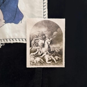 May include: A rectangular patch with a sepia-toned illustration of a skeletal figure on horseback, spearing figures on the ground. The patch is bordered by a white fabric with black stitching. The background is black.