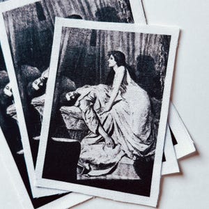 May include: Several rectangular fabric patches with a black and white image of a woman leaning over a man. The image depicts a classical scene with detailed shading and a dramatic composition. The patches are stacked, showing the edges of the fabric.