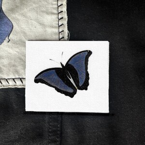May include: A blue butterfly with black outlines is printed on a white canvas patch.