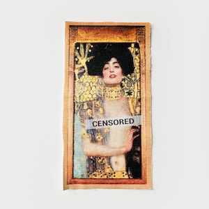 May include: Rectangular fabric patch featuring a portrait of a woman with black hair and a gold-colored necklace. The image is framed in a gold border and has the word "CENSORED" across the center.