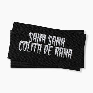 May include: Black woven fabric label with white text that reads "Sana Sana Colita de Rana".